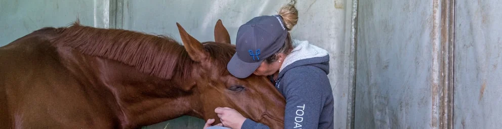 Cavalière enlaçant la tête de son cheval au box